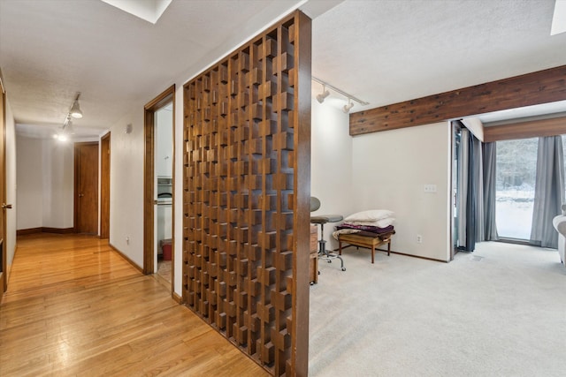 hall featuring rail lighting, light wood-type flooring, a textured ceiling, and beamed ceiling