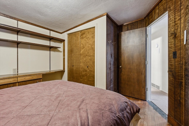 bedroom featuring light wood-type flooring, a textured ceiling, vaulted ceiling, and ornamental molding