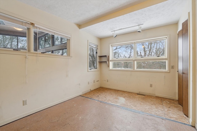 unfurnished room featuring track lighting, plenty of natural light, and a textured ceiling