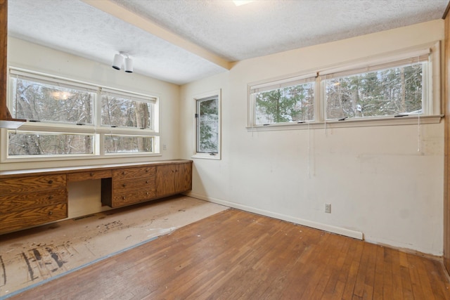 unfurnished room featuring built in desk, plenty of natural light, and a textured ceiling