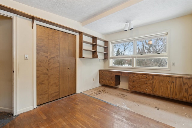 unfurnished office featuring wood-type flooring, a textured ceiling, and built in desk