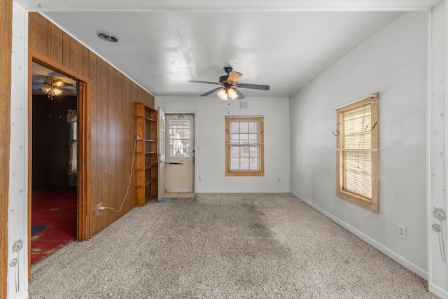 spare room featuring ceiling fan, wooden walls, and carpet