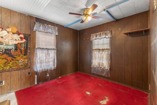 carpeted spare room featuring wood walls and ceiling fan