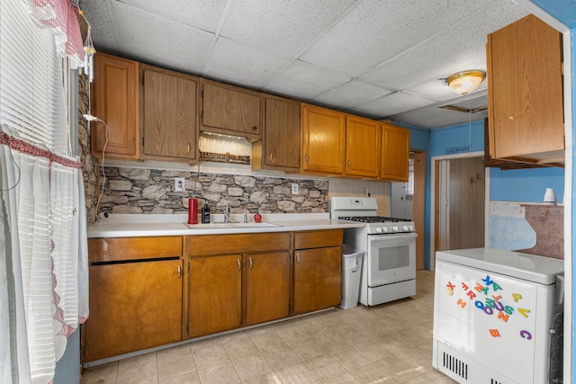 kitchen featuring white range with gas stovetop, a drop ceiling, refrigerator, and sink