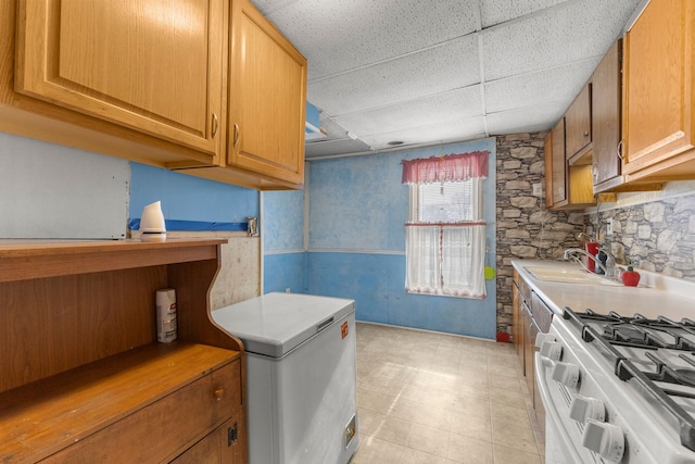 kitchen with stainless steel gas stove, refrigerator, sink, and a drop ceiling