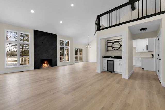 unfurnished living room featuring a chandelier, light hardwood / wood-style flooring, wine cooler, and a premium fireplace