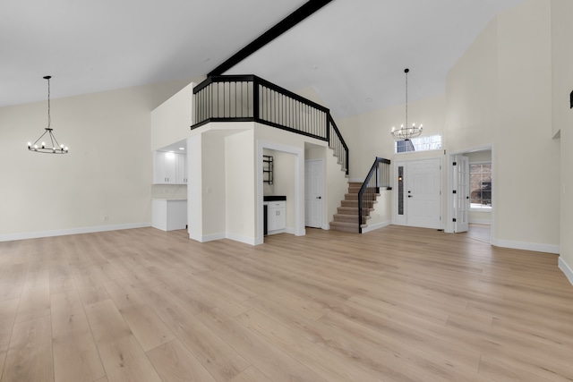 unfurnished living room featuring a towering ceiling, light hardwood / wood-style flooring, beam ceiling, and a notable chandelier