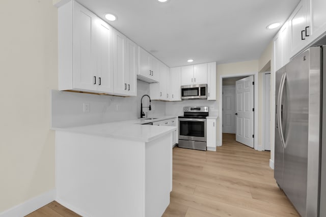 kitchen with sink, white cabinets, stainless steel appliances, and light wood-type flooring