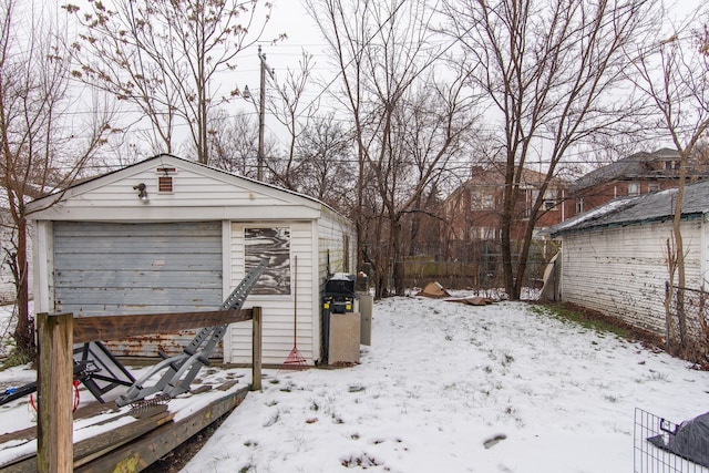 snowy yard with a garage and an outbuilding