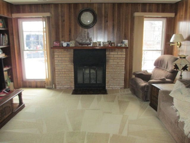 carpeted living room featuring a brick fireplace and wood walls