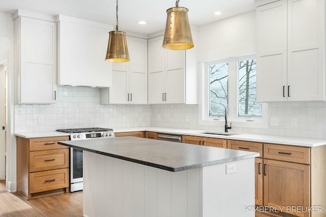 kitchen with appliances with stainless steel finishes, white cabinets, decorative light fixtures, a kitchen island, and sink