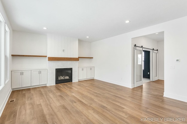 unfurnished living room with light hardwood / wood-style floors, a barn door, and a fireplace