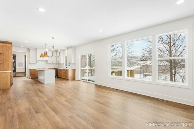 kitchen featuring stainless steel fridge, decorative light fixtures, white cabinetry, tasteful backsplash, and a center island