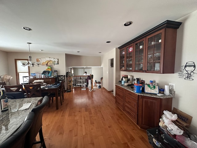 bar featuring pendant lighting, light stone counters, light hardwood / wood-style floors, a chandelier, and dark brown cabinetry