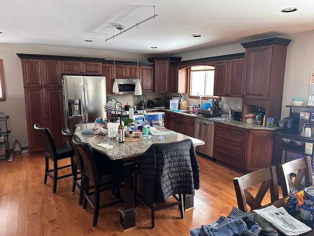 kitchen with hanging light fixtures, appliances with stainless steel finishes, light wood-type flooring, light stone countertops, and a kitchen island