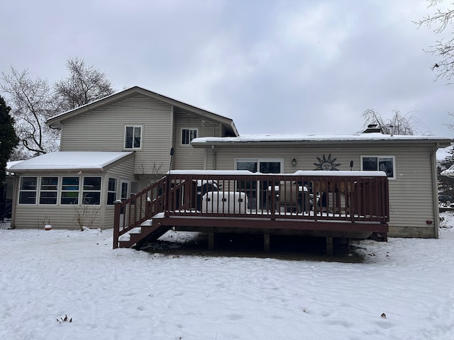 snow covered back of property with a sunroom and a deck