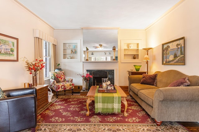 living area featuring ceiling fan, a fireplace, built in features, and ornamental molding