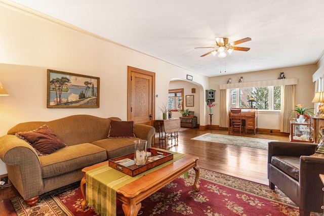 living area with ornamental molding, arched walkways, ceiling fan, and wood finished floors