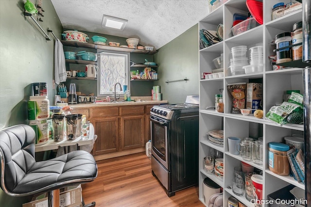 kitchen featuring a textured ceiling, lofted ceiling, sink, stainless steel stove, and light wood-type flooring