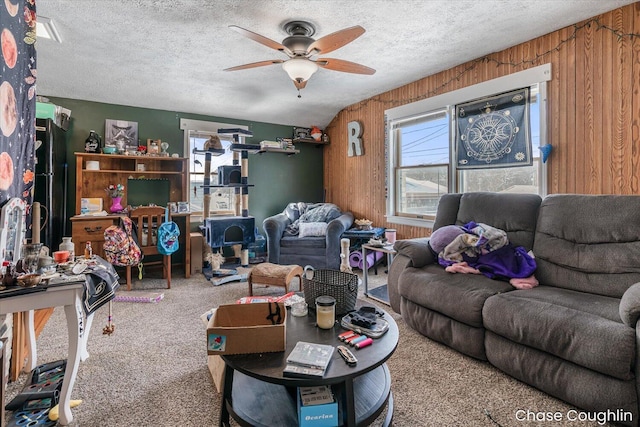 carpeted living room featuring ceiling fan, plenty of natural light, a textured ceiling, and wood walls