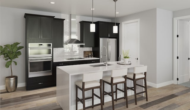 kitchen featuring appliances with stainless steel finishes, decorative light fixtures, backsplash, light wood-type flooring, and wall chimney range hood