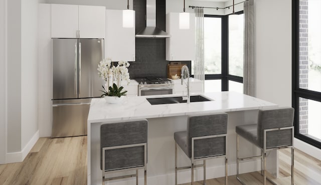 kitchen featuring pendant lighting, appliances with stainless steel finishes, wall chimney exhaust hood, a kitchen bar, and sink