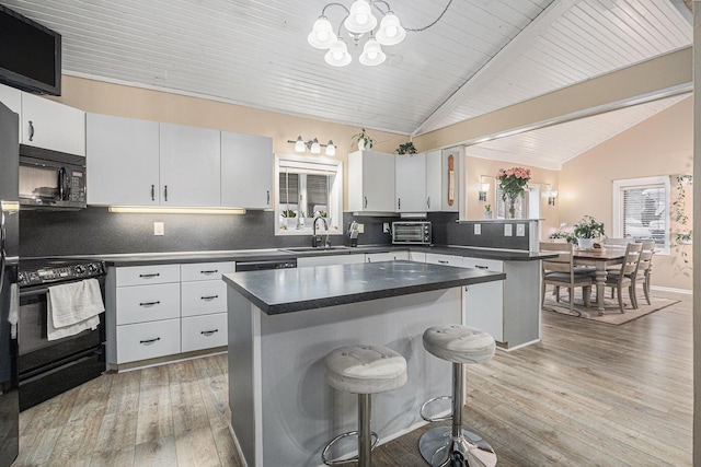 kitchen featuring a kitchen bar, vaulted ceiling with beams, a center island, black appliances, and decorative backsplash