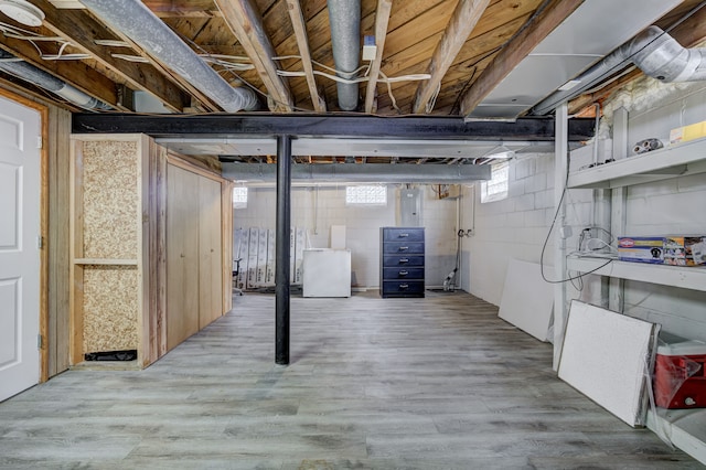 basement featuring white refrigerator, electric panel, and light wood-type flooring