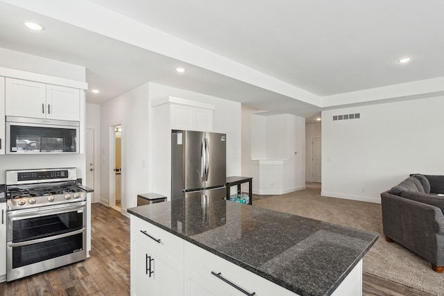 kitchen featuring stainless steel appliances, white cabinetry, a center island, and dark stone counters