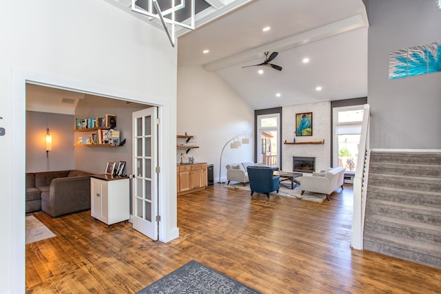 living room featuring ceiling fan, dark wood-type flooring, beamed ceiling, and a brick fireplace