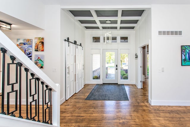 entryway featuring dark wood-type flooring, a towering ceiling, beam ceiling, a barn door, and coffered ceiling