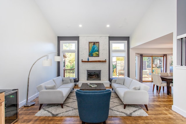 living room with a brick fireplace, hardwood / wood-style flooring, high vaulted ceiling, and a wealth of natural light