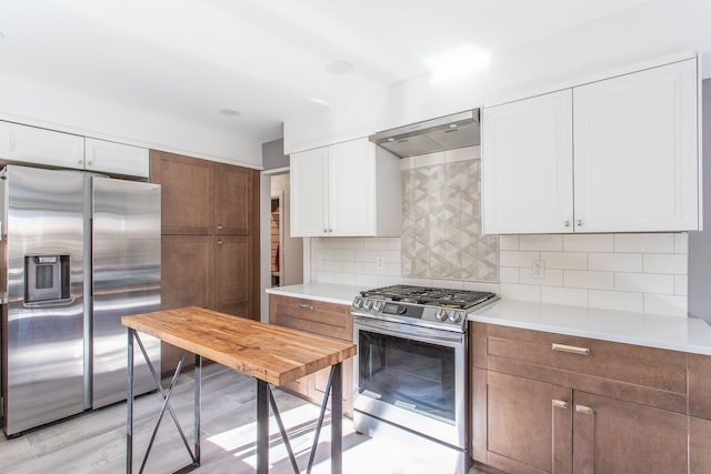 kitchen featuring wall chimney exhaust hood, white cabinets, decorative backsplash, and stainless steel appliances