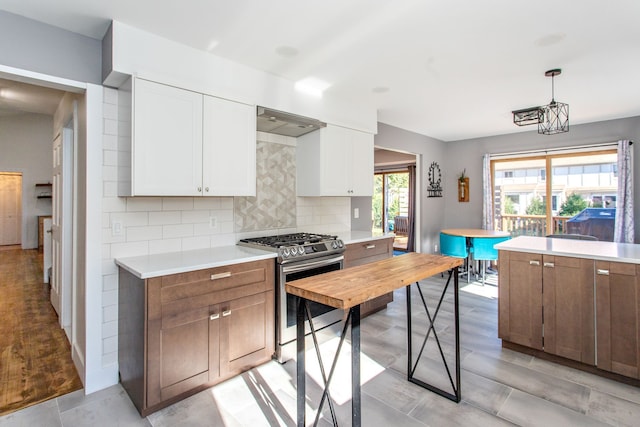 kitchen with stainless steel gas stove, decorative light fixtures, white cabinetry, and tasteful backsplash