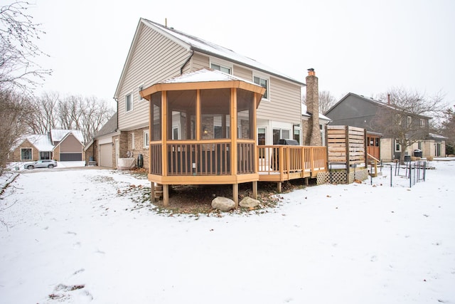 snow covered house with a garage, a deck, and a sunroom