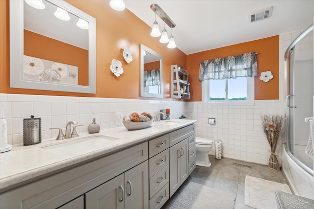 full bathroom featuring toilet, combined bath / shower with glass door, tile walls, tile patterned floors, and vanity