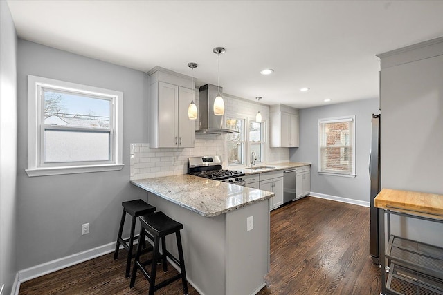 kitchen featuring wall chimney exhaust hood, sink, decorative light fixtures, white cabinetry, and stainless steel appliances