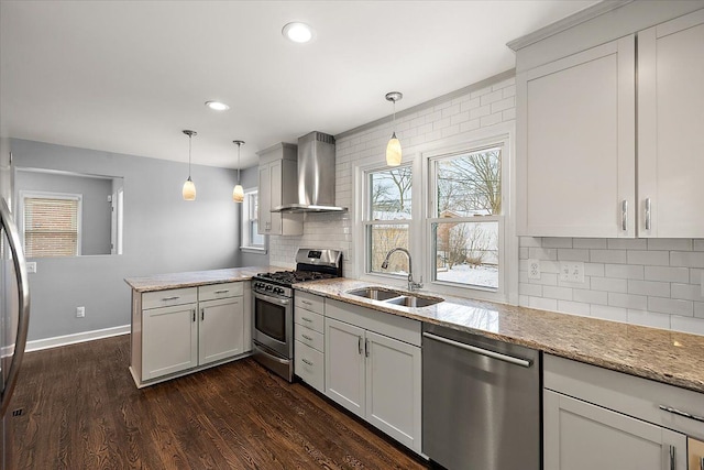 kitchen with wall chimney range hood, stainless steel appliances, sink, hanging light fixtures, and kitchen peninsula