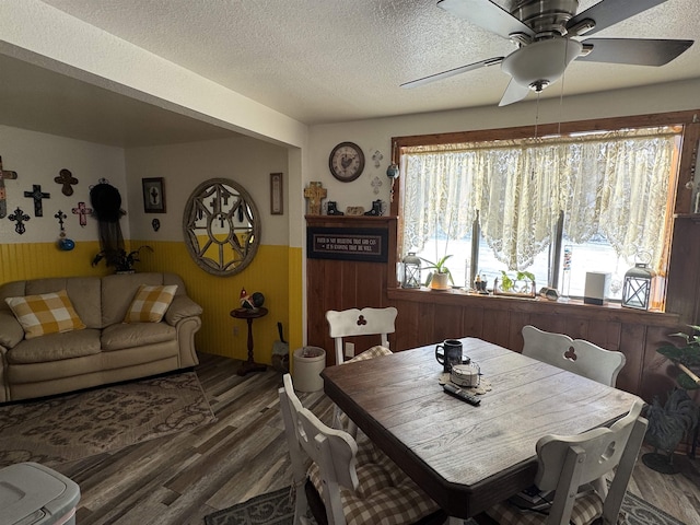 dining space featuring dark wood-type flooring, a textured ceiling, a healthy amount of sunlight, and wooden walls