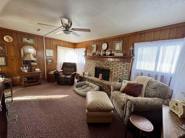 living room with ceiling fan, a brick fireplace, carpet, a textured ceiling, and wooden walls