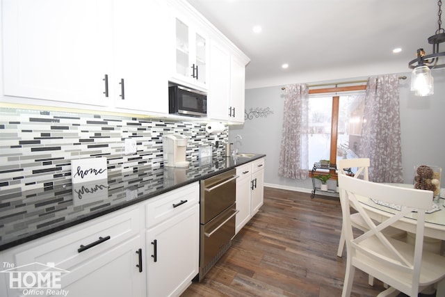 kitchen with white cabinets, decorative light fixtures, dark wood-type flooring, sink, and backsplash