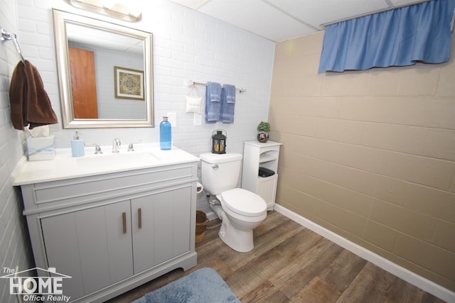 bathroom featuring brick wall, a paneled ceiling, vanity, toilet, and hardwood / wood-style flooring