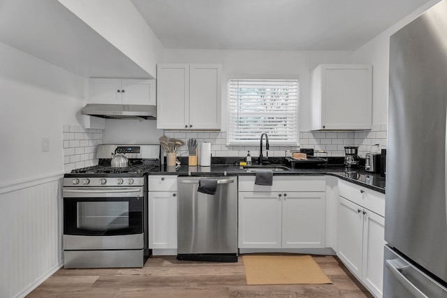 kitchen featuring white cabinets, stainless steel appliances, dark stone counters, light hardwood / wood-style floors, and sink