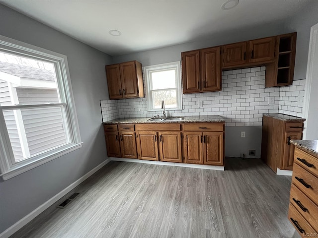 kitchen with sink, light hardwood / wood-style floors, decorative backsplash, and light stone countertops