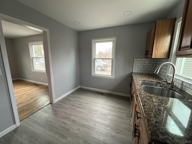 kitchen with sink, dark stone countertops, a wealth of natural light, and light hardwood / wood-style flooring