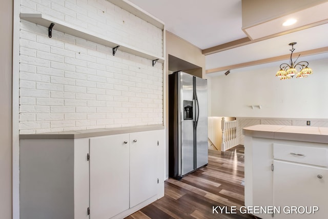 kitchen with brick wall, hanging light fixtures, white cabinets, and stainless steel fridge with ice dispenser