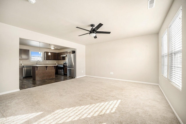 unfurnished living room featuring ceiling fan, sink, and dark colored carpet