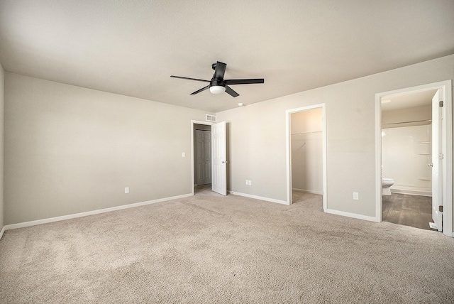 unfurnished bedroom with a spacious closet, a closet, carpet flooring, ceiling fan, and ensuite bathroom