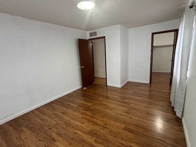 unfurnished bedroom featuring a walk in closet, dark hardwood / wood-style floors, a closet, and a textured ceiling