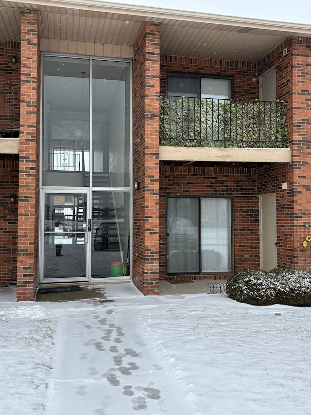 snow covered property entrance featuring a balcony